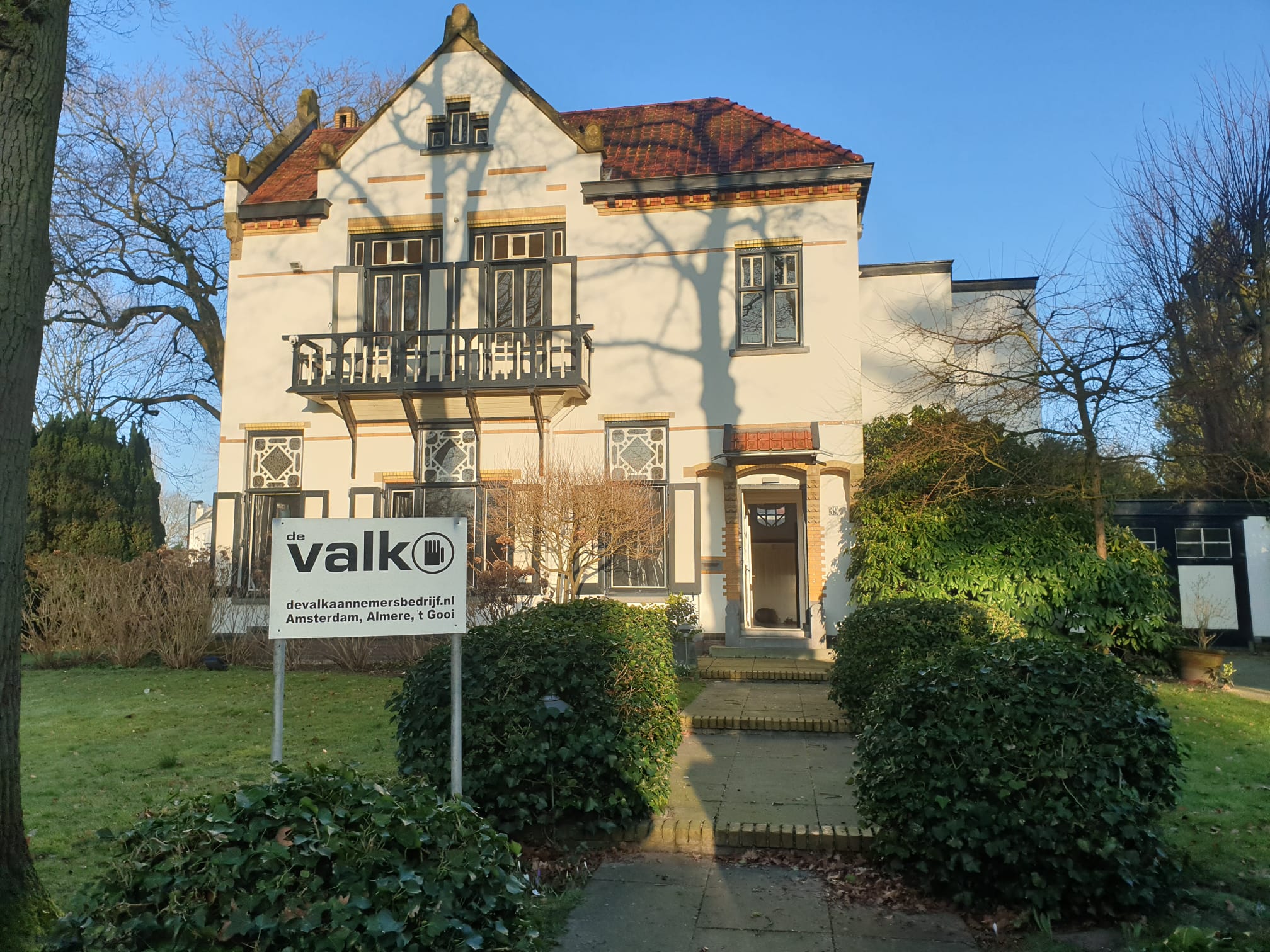 Prachtig groot huis met cremé kleur en een bord met de Valk in de tuin